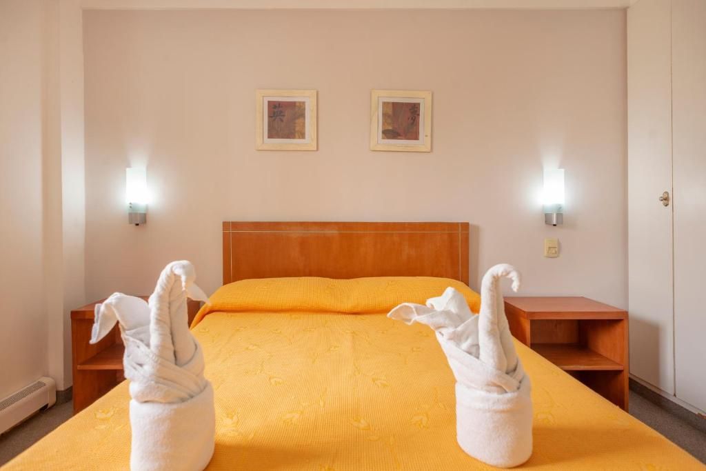 A hotel room with a single bed, two wall-mounted lights, and two framed pictures on the wall.