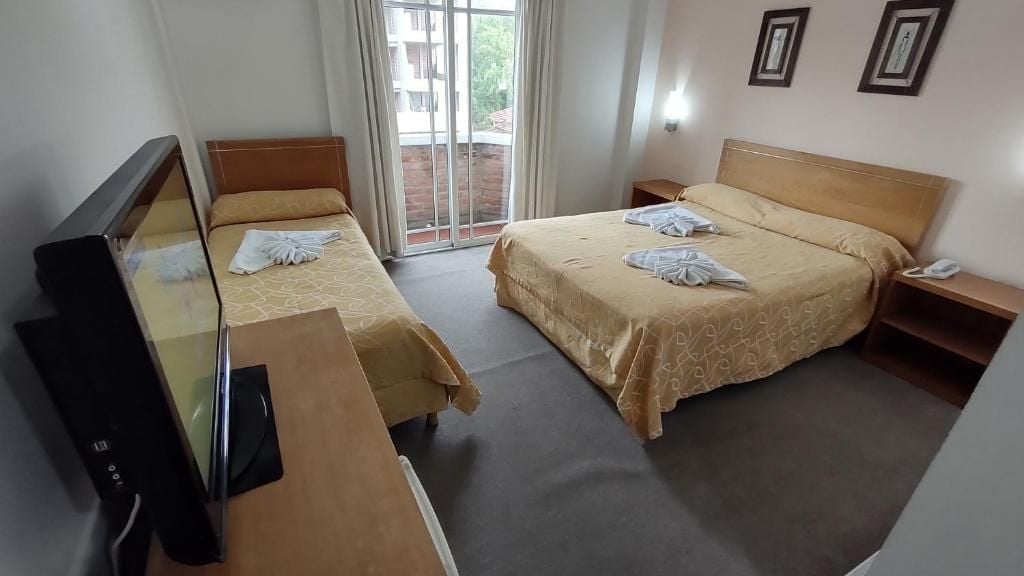 A hotel room with two single beds, a TV, a desk, and a sliding glass door to the outside.