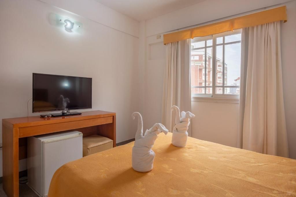 A hotel room with a bed, a television, a small refrigerator, and a window with curtains.