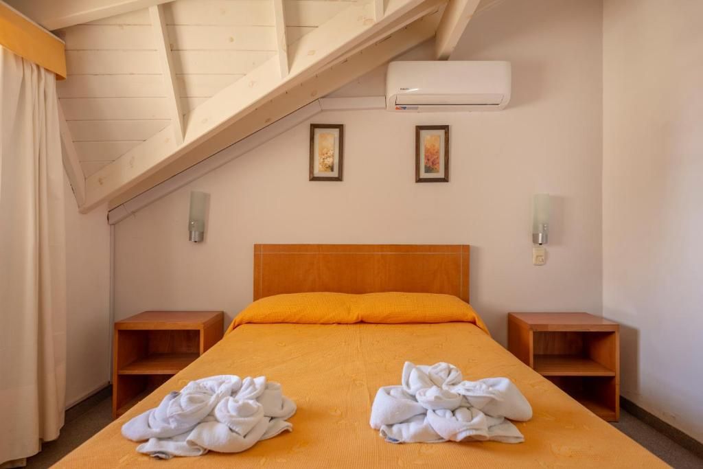 Un lit simple avec une tête de lit orange, dans une pièce dont le plafond est orné de poutres en bois. Il y a deux tables de chevet, une de chaque côté du lit.