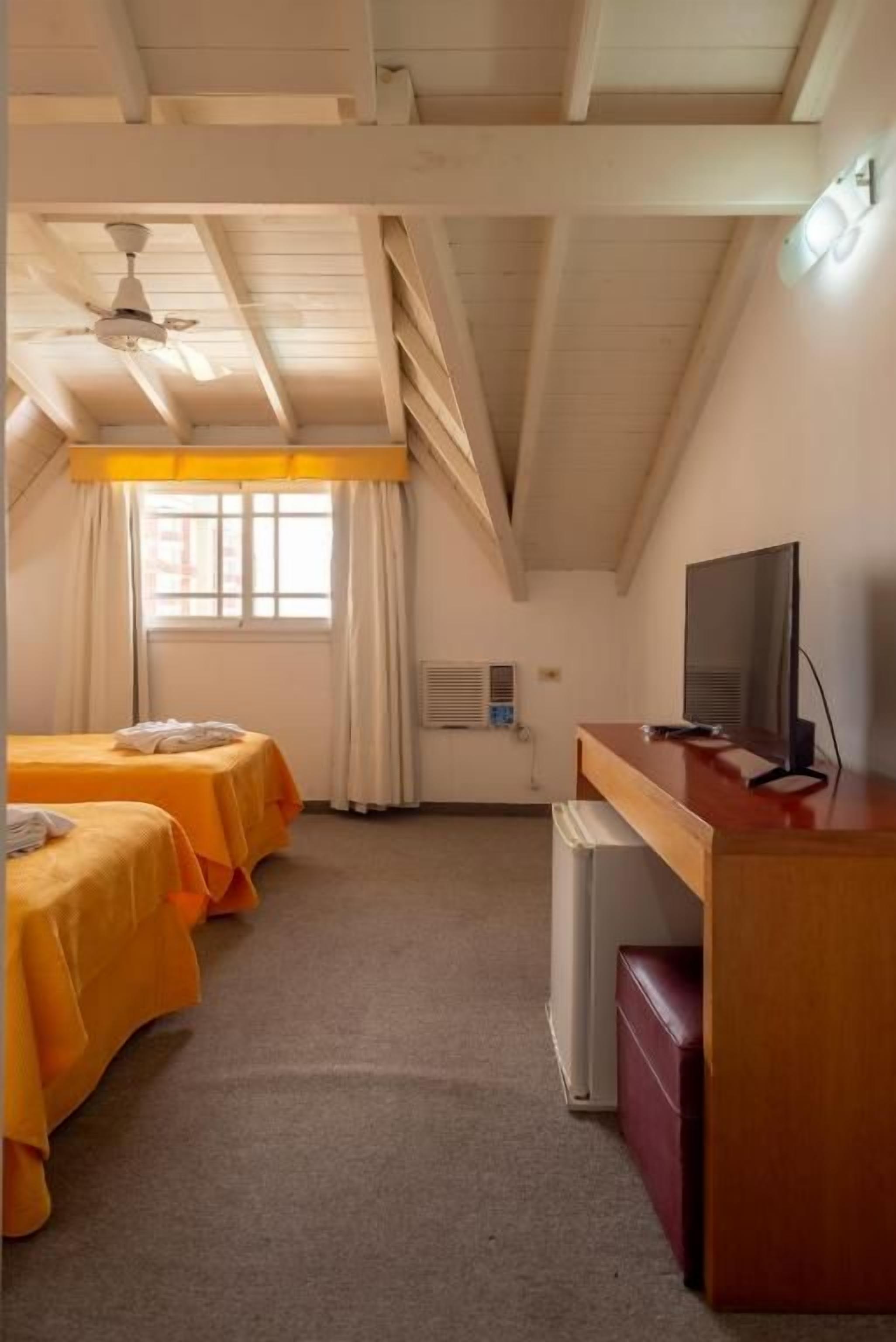 Ein Hotelzimmer mit zwei Betten, einem Schreibtisch, einem Fernseher und einem Vorhangfenster.