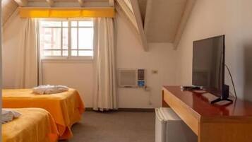 Ein Hotelzimmer mit zwei Betten, einem Schreibtisch, einem Fernseher und einem Vorhangfenster.