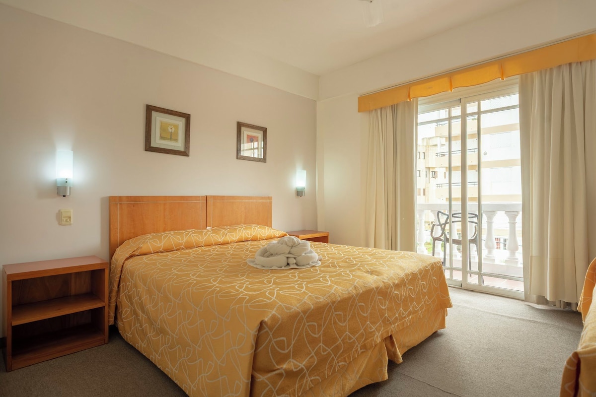 A hotel room with a bed, bedside tables, a window with curtains, and a balcony.