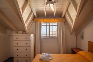 Una habitación de hotel con cama, cómoda, ventana con cortinas y ventilador de techo.