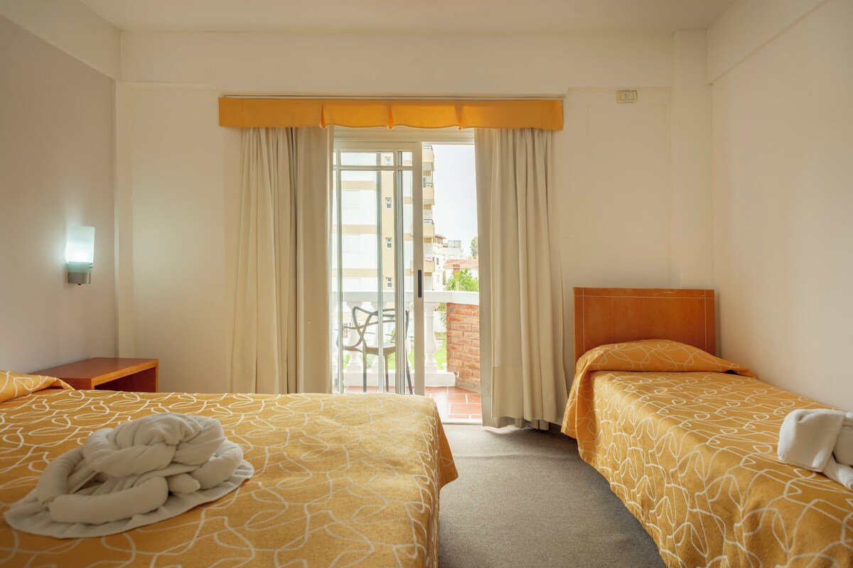 A hotel room with two beds, a balcony, and a view of buildings.