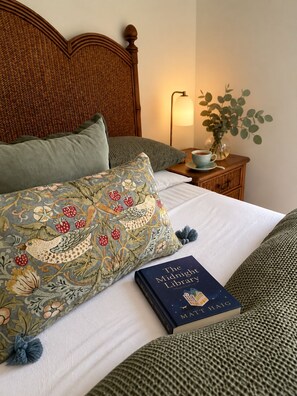 A neatly made bed with a patterned pillow and a book titled 'The Midnight Library' by Matt Haig.