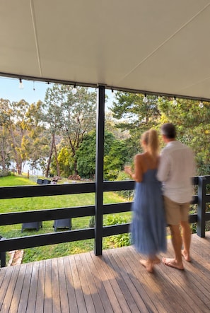 A covered outdoor area with a wooden deck, a black fence, and a view of trees and grass.