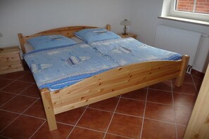 A wooden bed with a blue quilt, a bedside table with a lamp, and a window with a view of a brick wall. - "Sunshine" at the Müritz (Sietow)
