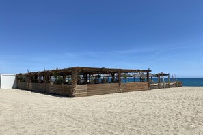 Eine am Strand stehende Holzkonstruktion mit einem Reetdach, umgeben von einem Holzzaun und mit Blick aufs Meer.