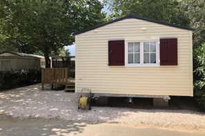 A single-story mobile home with a flat roof, a front porch, and a window with shutters. - Chalet à la maison camping club (Argeles sur mer)