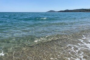 A clear view of a beach with shallow water, pebbles, and distant hills. - Chalet à la maison camping club (Argeles sur mer)
