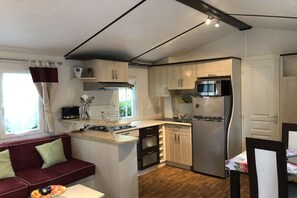Eine kleine Küche mit Herd, Mikrowelle und Kühlschrank, ein Essbereich mit Tisch und Stühlen sowie ein rotes Sofa mit Kissen.