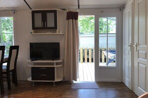 Ein Zimmer mit einem Fernseher auf einem weißen Schrank, einer Tür zu einem Balkon und einem Holzboden.