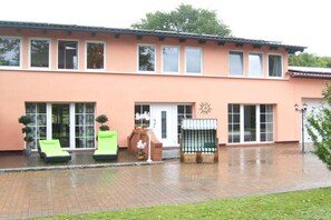 Ein zweistöckiges Gebäude mit Ziegelterrasse, überdachter Sitzgruppe und einem großen Fenster mit Sonnendekoration.
