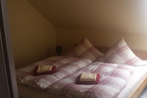 A bed with a plaid bedspread and pillows, a nightstand with a lamp, and a window with blinds. - Holiday apartment with 1 bedroom (Schwielochsee)
