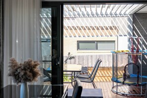 Ein modernes Interieur mit einer Glastür, die zu einem Außenbereich mit einer Holzterrasse, einem Trampolin und einer Kletterkonstruktion führt.