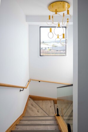 Eine moderne Treppe mit Holzstufen und einer Glasreling, die zu einem Raum mit einem großen Fenster mit Blick auf eine Wohngegend führt.