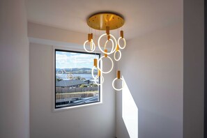 Ein Zimmer mit großem Fenster und Blick auf eine Landschaft, einer modernen Pendelleuchte und einer Wasserfläche.