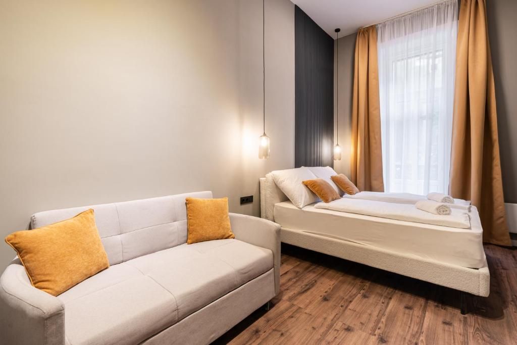 A modern hotel room with a sofa, a bed, and a window with curtains.