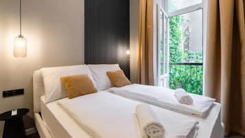 Een hotelkamer met een bed, nachtkastje, hanglamp en een raam met gordijnen.