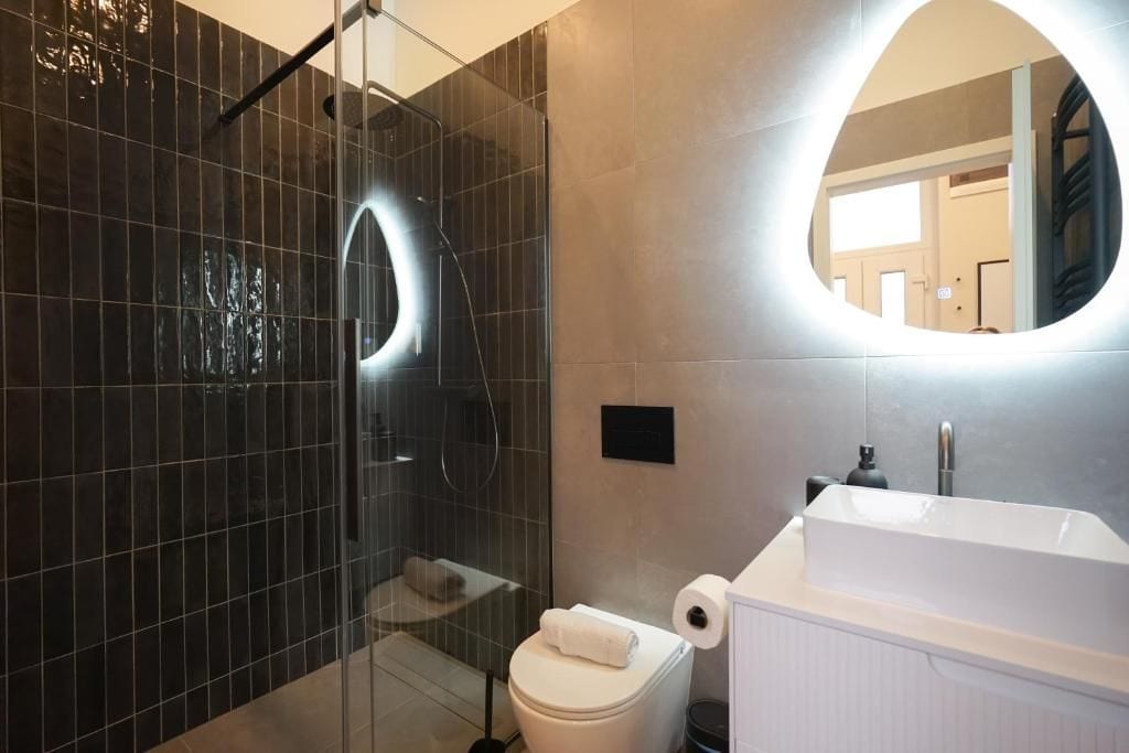 A modern bathroom with a glass-enclosed shower, a white sink, and a round mirror.