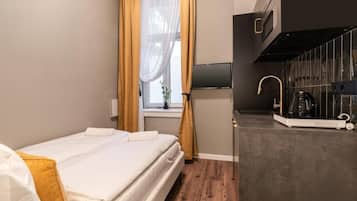 Quarto de hotel com cama, janela com cortinas, televisão de tela plana, área de cozinha com cafeteira e micro-ondas.