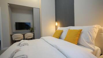 Una habitación de hotel moderna con una cama, un televisor de pantalla plana, un escritorio con dos sillas y una lámpara de pared.