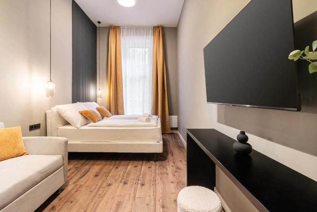 A modern hotel room with a bed, a sofa, a TV, and a plant.