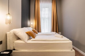A hotel room with a bed, a bedside lamp, a window with curtains, and a small table with a book. - S7- Síp Downtown Hideaway by BQA (Budapest)