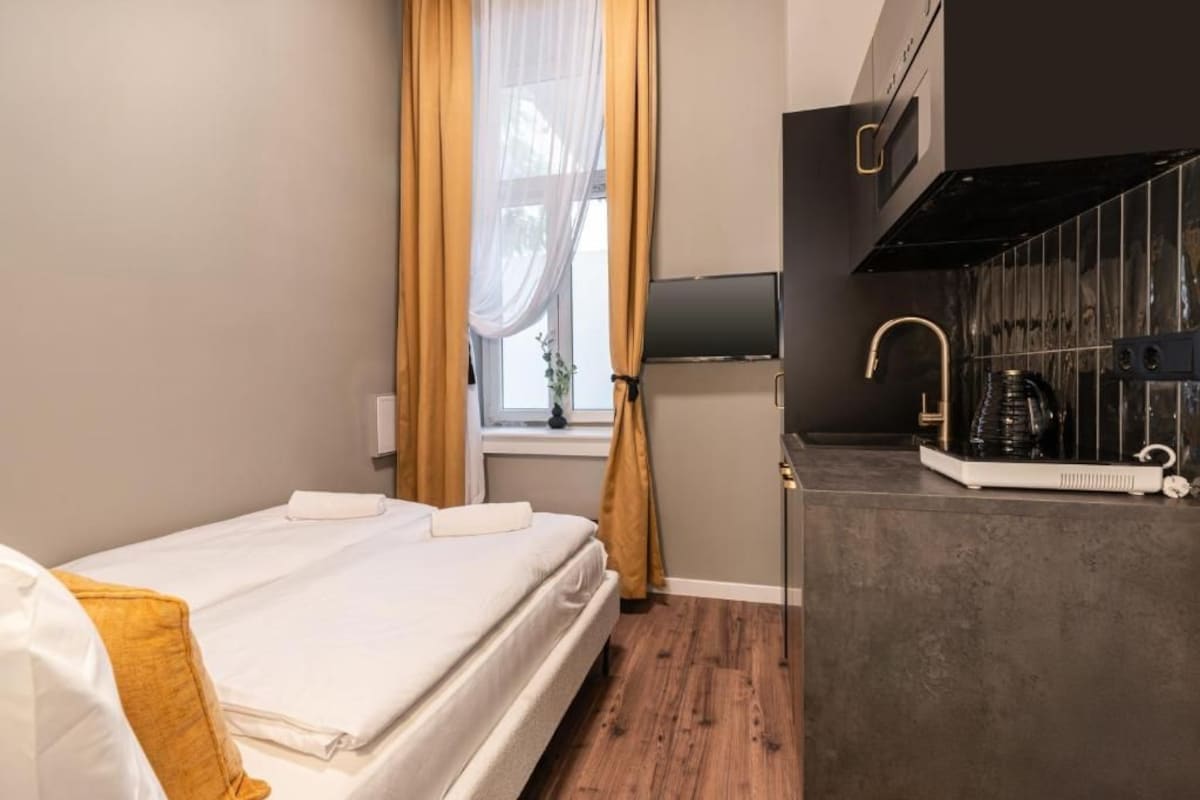 Hotelkamer met een bed, een raam met gordijnen, een flatscreen televisie, een keukenhoek met een koffieapparaat en een magnetron.