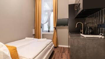 A hotel room with a bed, a window with curtains, a flat-screen TV, a kitchen area with a coffee machine, and a microwave.