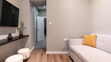 Een moderne woonkamer met een bank, poefs, een flatscreen televisie en een plant.
