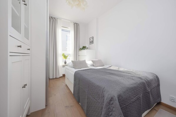 A bedroom with a bed, a bedside table with a lamp, a window with curtains, and a wardrobe. - Warsaw | Silnikowa 15 | Modern Apartment | Desk | Balcony (Warszawa)
