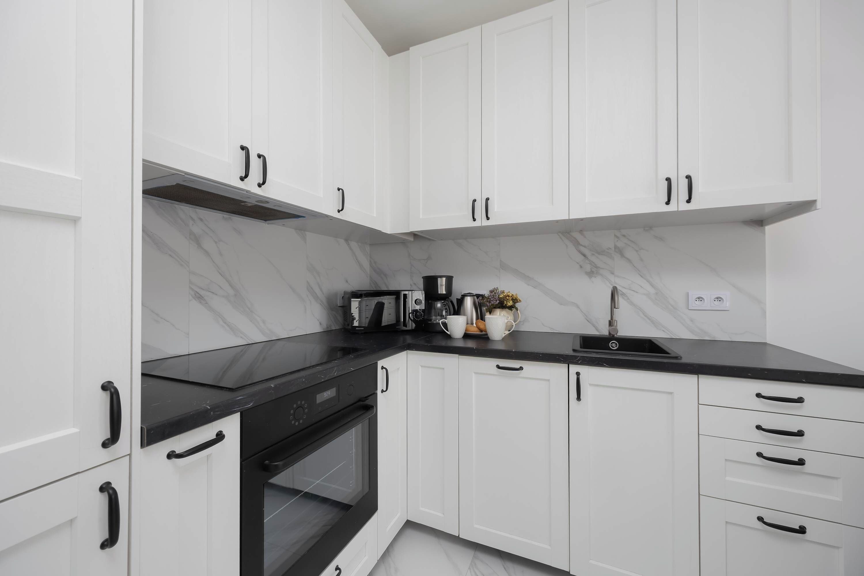 A modern kitchen with white cabinets, black countertops, and a built-in oven.