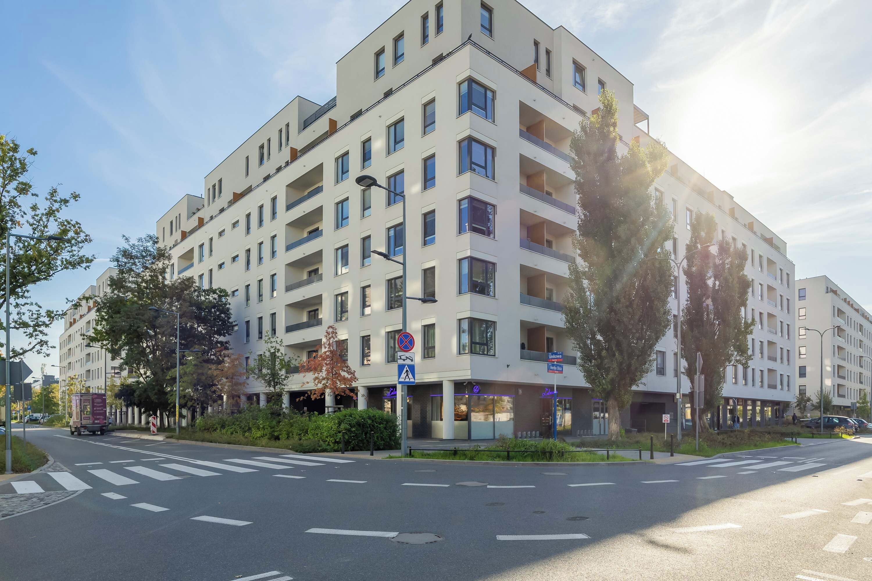 Un edificio residencial de varios pisos con balcones, un paso de peatones y una calle con carriles señalizados.
