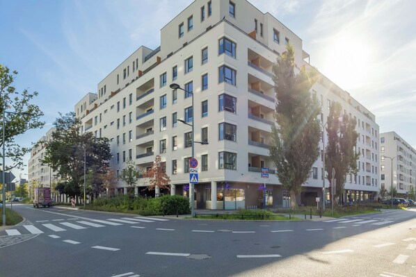 A multi-story residential building with balconies, a pedestrian crossing, and a street with marked lanes. - Warsaw | Silnikowa 15 | Modern Apartment | Desk | Balcony (Warszawa)