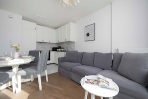 Una sala moderna con un sofá gris, una mesa de comedor con sillas, y una cocina al fondo.