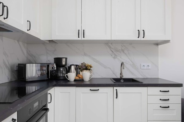 Una cocina moderna con armarios blancos, encimera negra, horno empotrado, microondas, cafetera y fregadero.