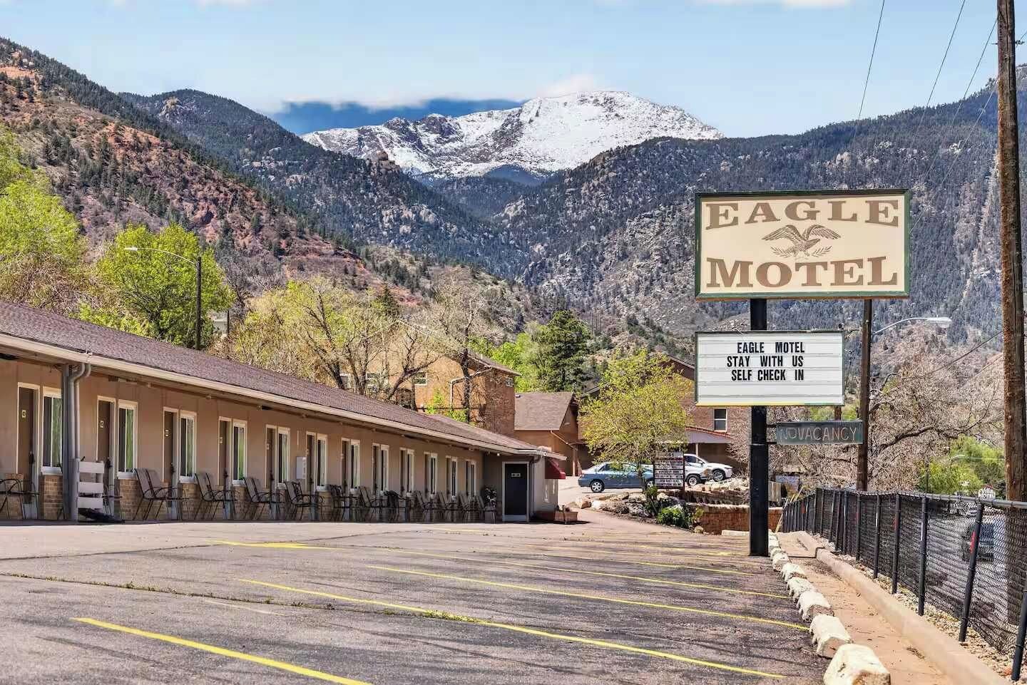 Un motel avec un panneau indicateur, un espace de stationnement et un paysage montagneux en arrière-plan.