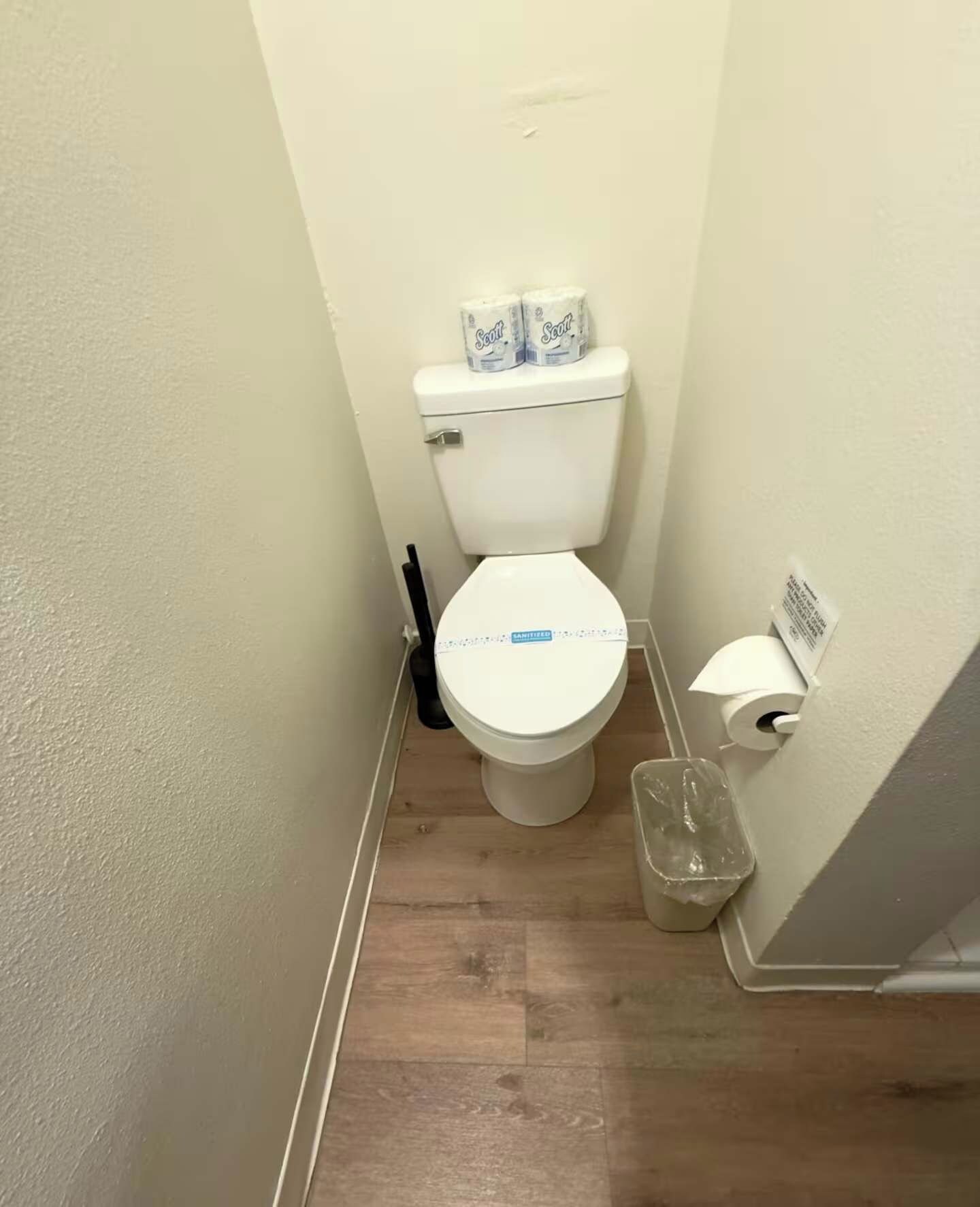 Um banheiro pequeno com vaso sanitário, lixeira e porta-papel higiênico.