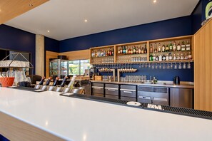A bar area with a long counter, shelves with bottles, and glasses.