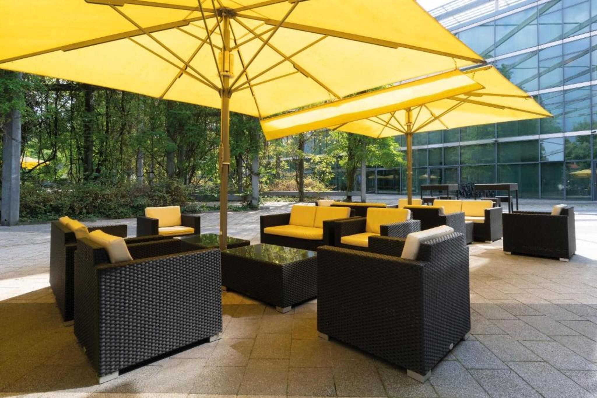 Sitzgelegenheiten im Freien mit gelben Sonnenschirmen, schwarzer Rattanmöbel und einem Glasgebäude im Hintergrund.