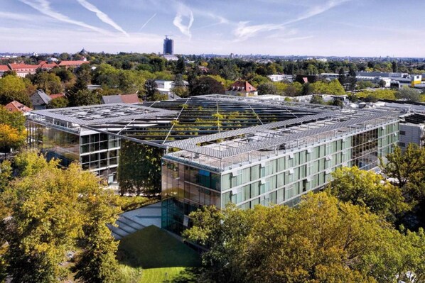 Un edificio moderno con techo plano, rodeado de árboles y otros edificios.