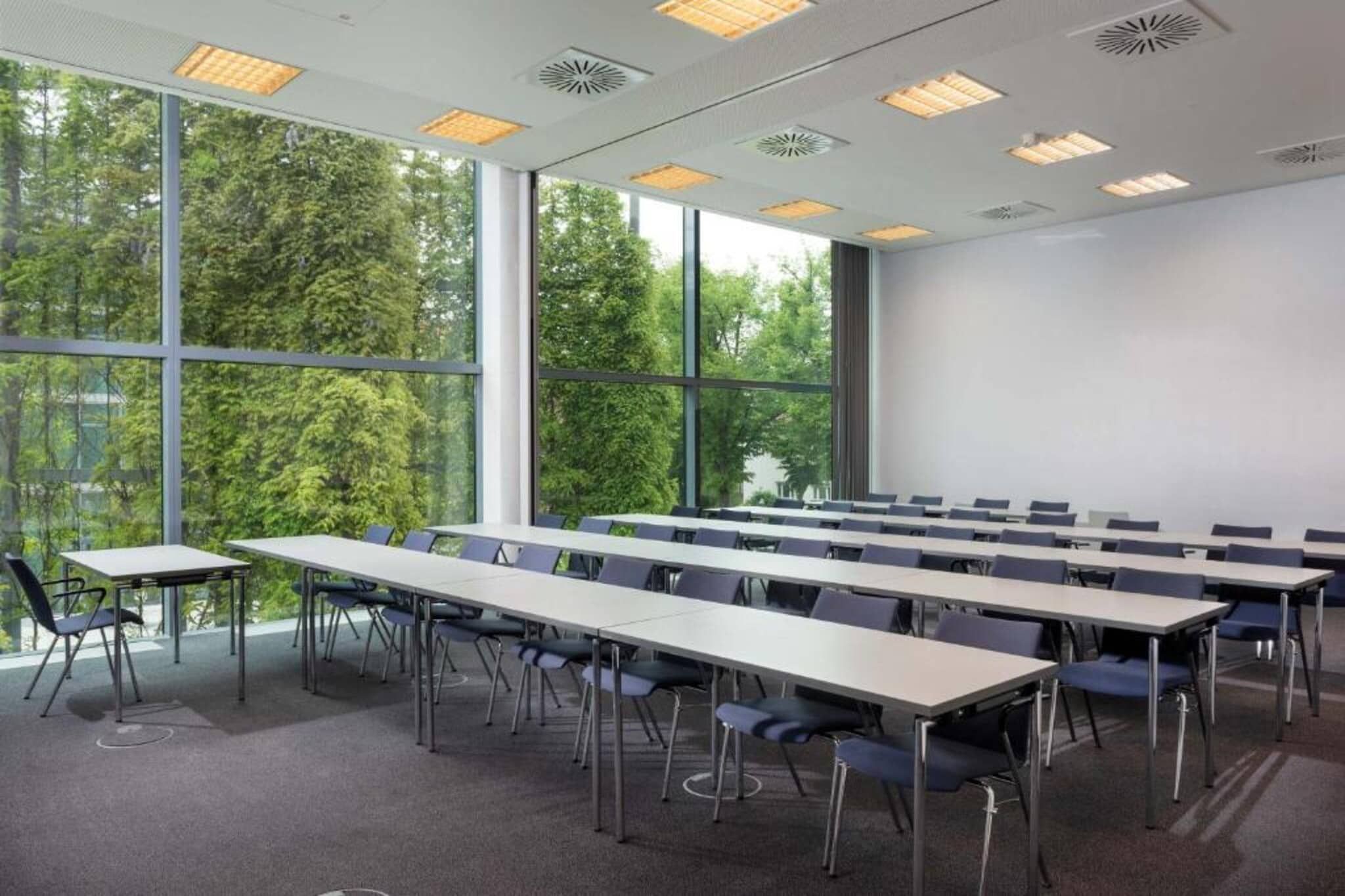 A conference room with tables and chairs, large windows, and ceiling lights.