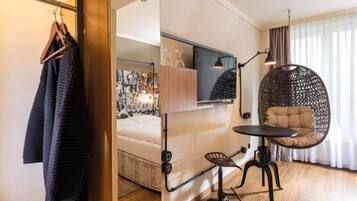 Una habitación de hotel moderna con cama, escritorio con silla, sillón colgante y armario con ropa.