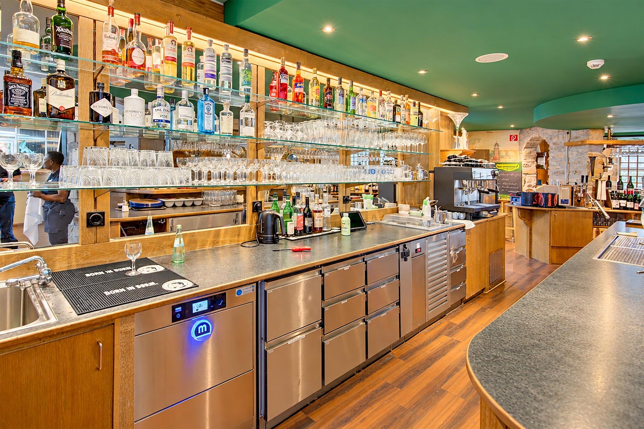 Zona de bar amb estantes plenes de botelles de licors, una màquina de cafè i una balança digital.