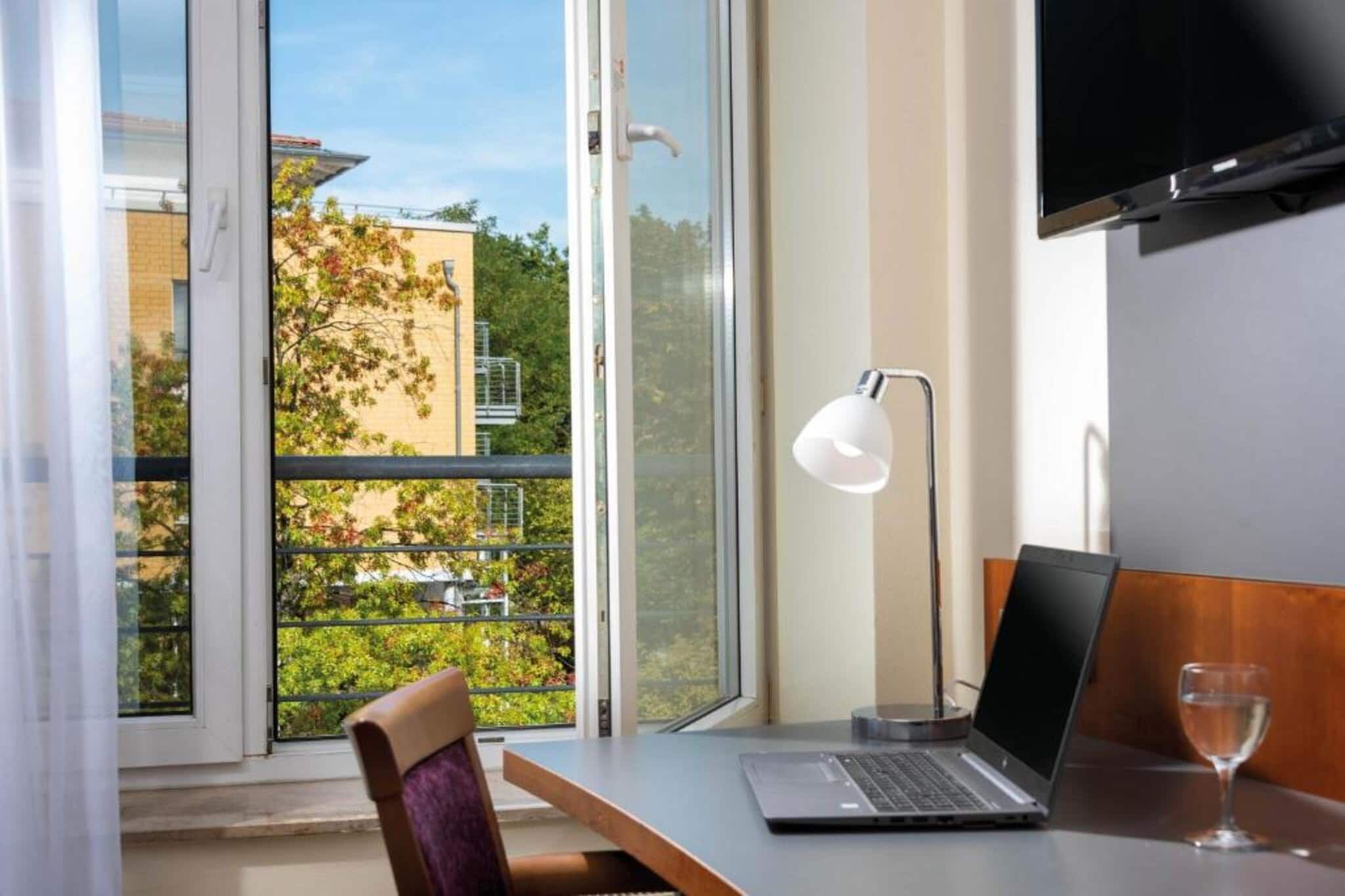 A room with a laptop on a table, a chair, a desk lamp, and a glass of water.