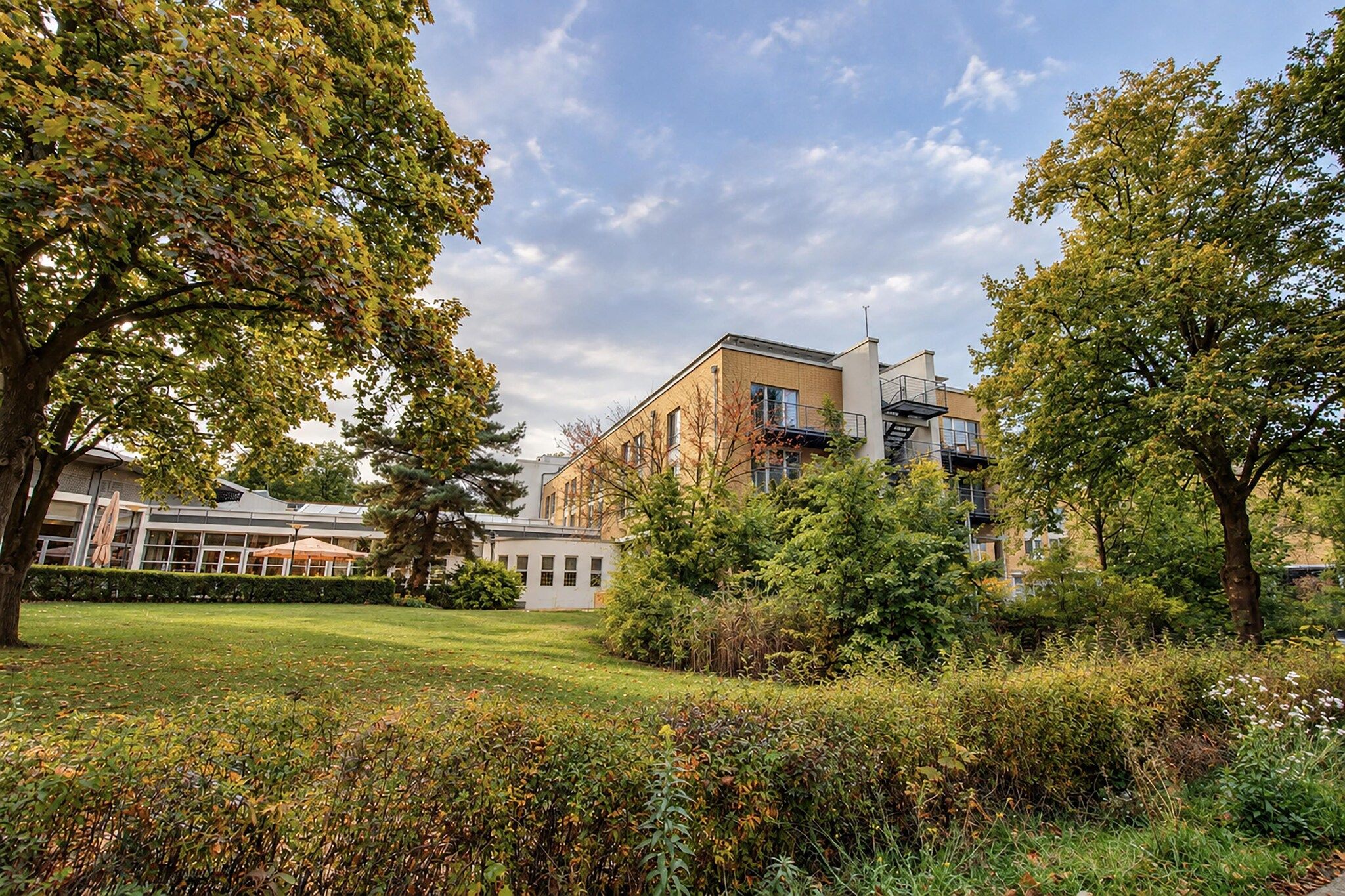 Ein Gebäude im modernen Baustil, umgeben von einem gepflegten Garten mit verschiedenen Sträuchern und Bäumen.