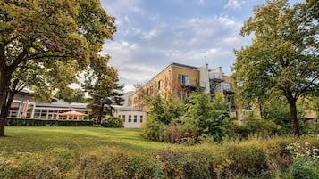 Ein Gebäude im modernen Baustil, umgeben von einem gepflegten Garten mit verschiedenen Sträuchern und Bäumen.