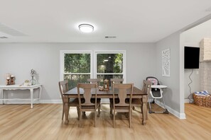 A dining area with a table and chairs, a window with a view of trees, a white console table with decorative items, and a wall-mounted TV. - Houston Co Lakefront - Dock, Games, Views (Crockett)